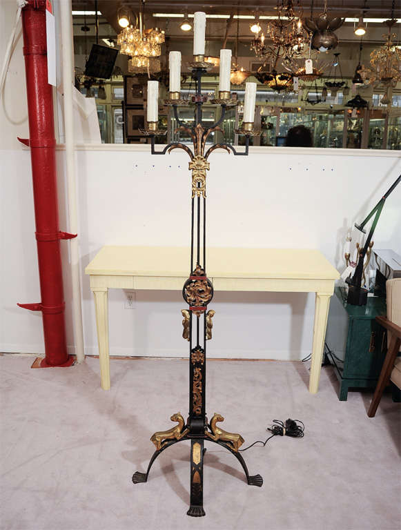 An early 19th Century Gothic Revival style standing candelabra converted to a floor lamp. In wrought iron with red accents and bronze appliques depicting grotesque masks, lions and praying women.<br />
<br />
Reduced From: $4,750