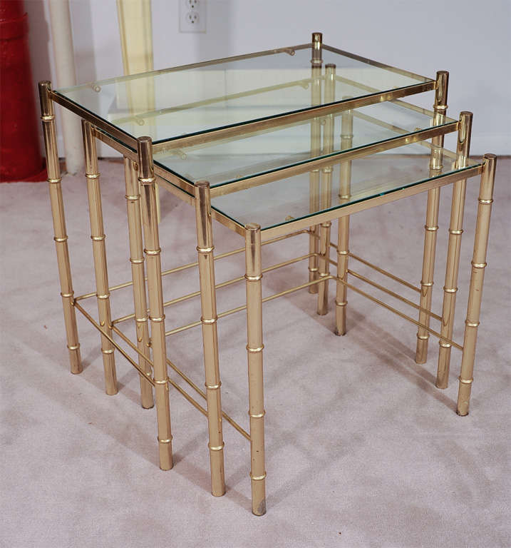 A set of three brass nesting table with faux bamboo legs and glass tops.<br />
Larger Table: 20