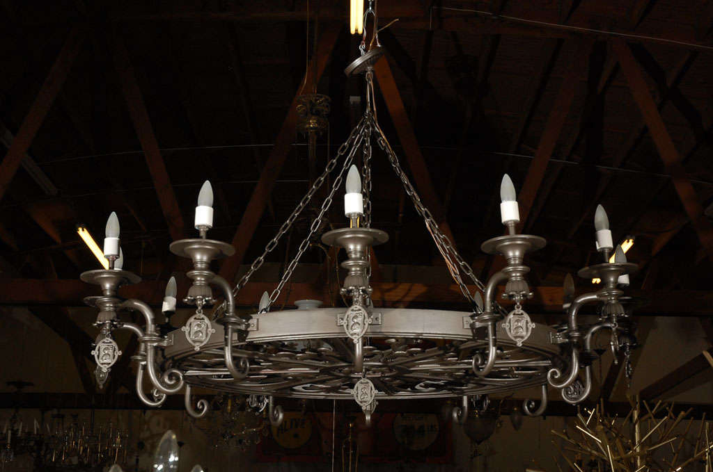 This fixture is thought to be French, circa the 1920-30's. It has 12 up lights arranged on a circular frame and is suspended by chains. Decorative elements would suggest it is from a medieval castle, were it older. Jefferson West antiques offer a