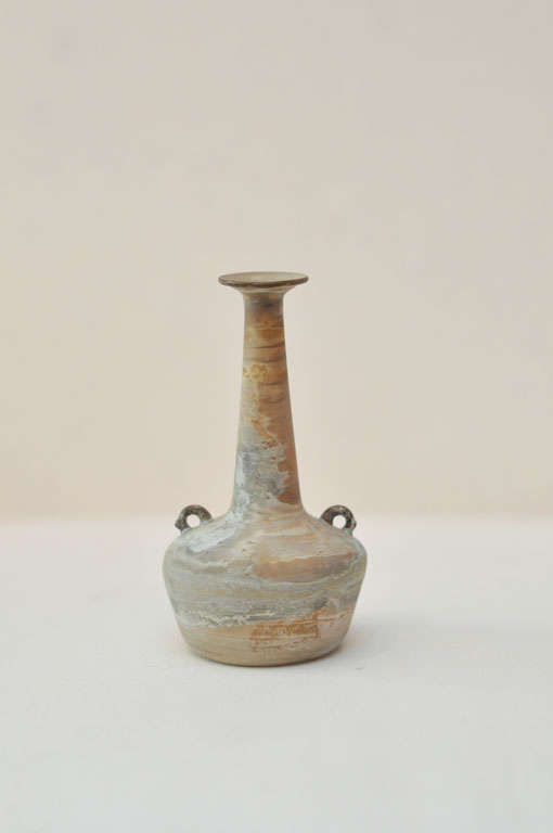 Museum quality ungentarium bottle which was used to hold scented oils or cosmetics. The glass has an unusual, cloudy patina with areas of brown, gray and green.