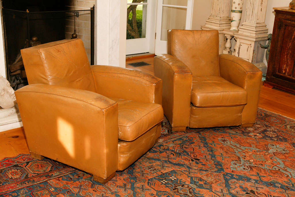 In the spirit of Jean-Michel Frank this pair of French leather<br />
club chairs have his classic rectalinear lines. The leather is <br />
well worn. Call for condition details.