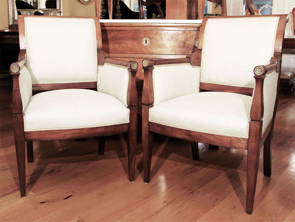 Clean, fluid and restrained lines best define this handsome pair of Directoire solid walnut bergeres (closed armchairs) with bronze medallions finishing each arm. Found in completely original condition, recently reupholstered in a light colored sea