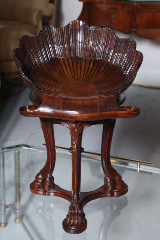 Naturalistically carved shell-shaped adjustable seat on cabriole legs with claw feet joined by a concave-sided plinth.