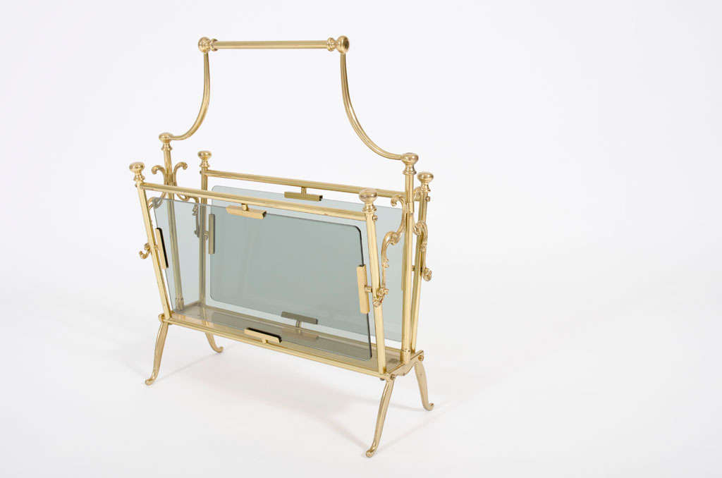 A pared down Victorian style magazine stand in polished brass with flattened ball finials, laurel leaf appliqués and pale green sea glass side panels. With label 