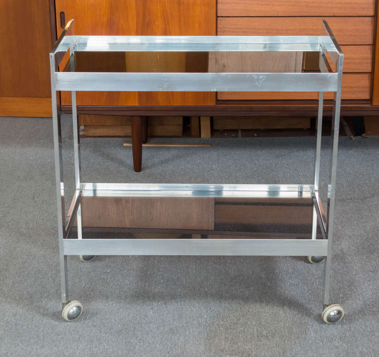 Offering a 1970s Polished aluminum two tiered smoked glass bar cart.  The maker is unknown but the quality is very good and feels very much in the vein of Paul Mayen for Habitat.