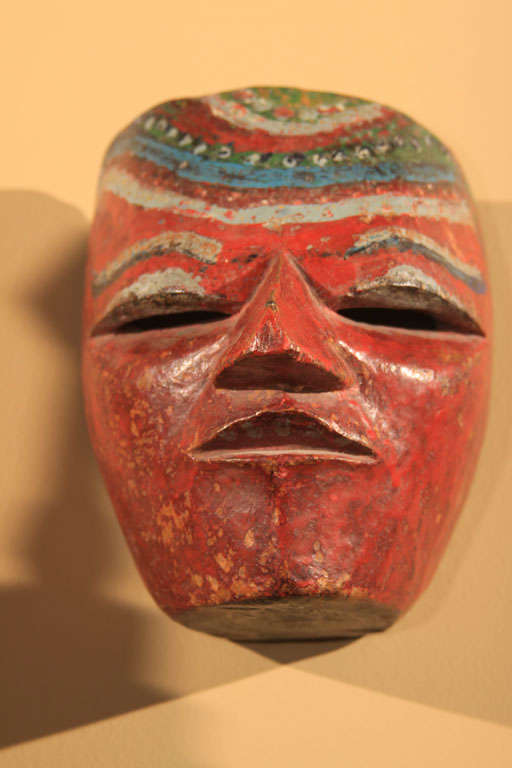 Javanese carved and painted wood dance mask from the Dieng Plateau region in central Java, Indonesia. The face with narrow, pierced eyes, straight nose and slightly open mouth. Red pigment ground with curving bands of blue, white and green on the