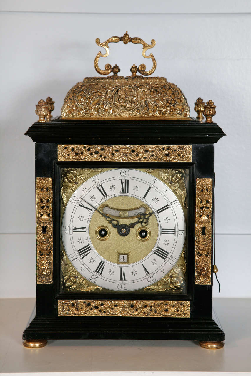 An exceptional William & Mary period ebony repoussé basket-top striking bracket clock. The moulded ebony veneered case has four gilt swag and urn repoussé mounts to the front door and is surrounded by a similar gilt one piece pierced basket top