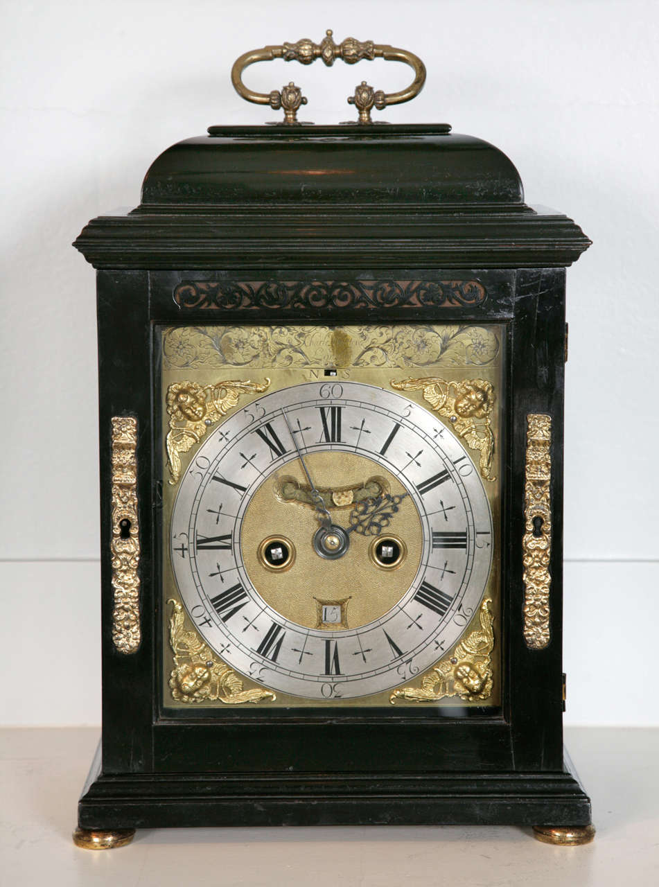 A fine Queen Anne period ebony veneered table clock by this celebrated maker, Charles Gretton. 

The elegant case is veneered with ebony on an oak carcase and has an elegant domed caddy-top, with a knopped and chased gilt brass carrying handle and
