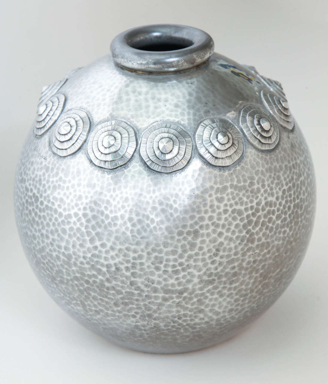 Spherical pewter vase with 12 applied circular designs around the neck and with ring collar.

Signed R. Delavan/ Impressed underneath R. DELAVAN/ DECORATEUR/ PARIS/ ETAIN D'ART/ DEPOSE