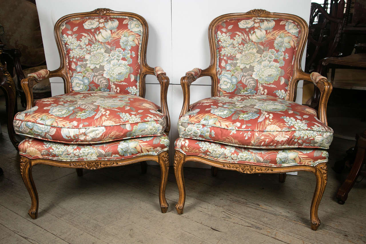 This pair of fruitwood framed open armchairs, or fauteuils are in the Louis XV style and date from the mid-20th century. They have been recently reupholstered in what appears to be cotton. Hand-carved frame with hand carvings adorning the crest