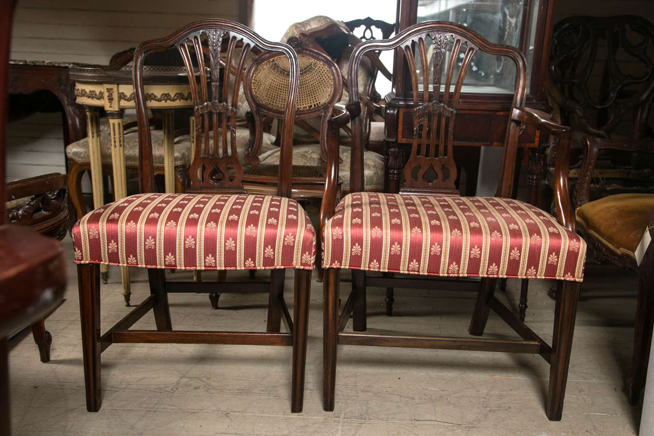 This set of 8 chairs in the Hepplewhite manner consists of  2  arm chairs and  6  side chairs.  The top rail have a gently curving arch and rounded corners. The 5 part back splat is carved with lily of the valley flowers. The rear  legs splay out a