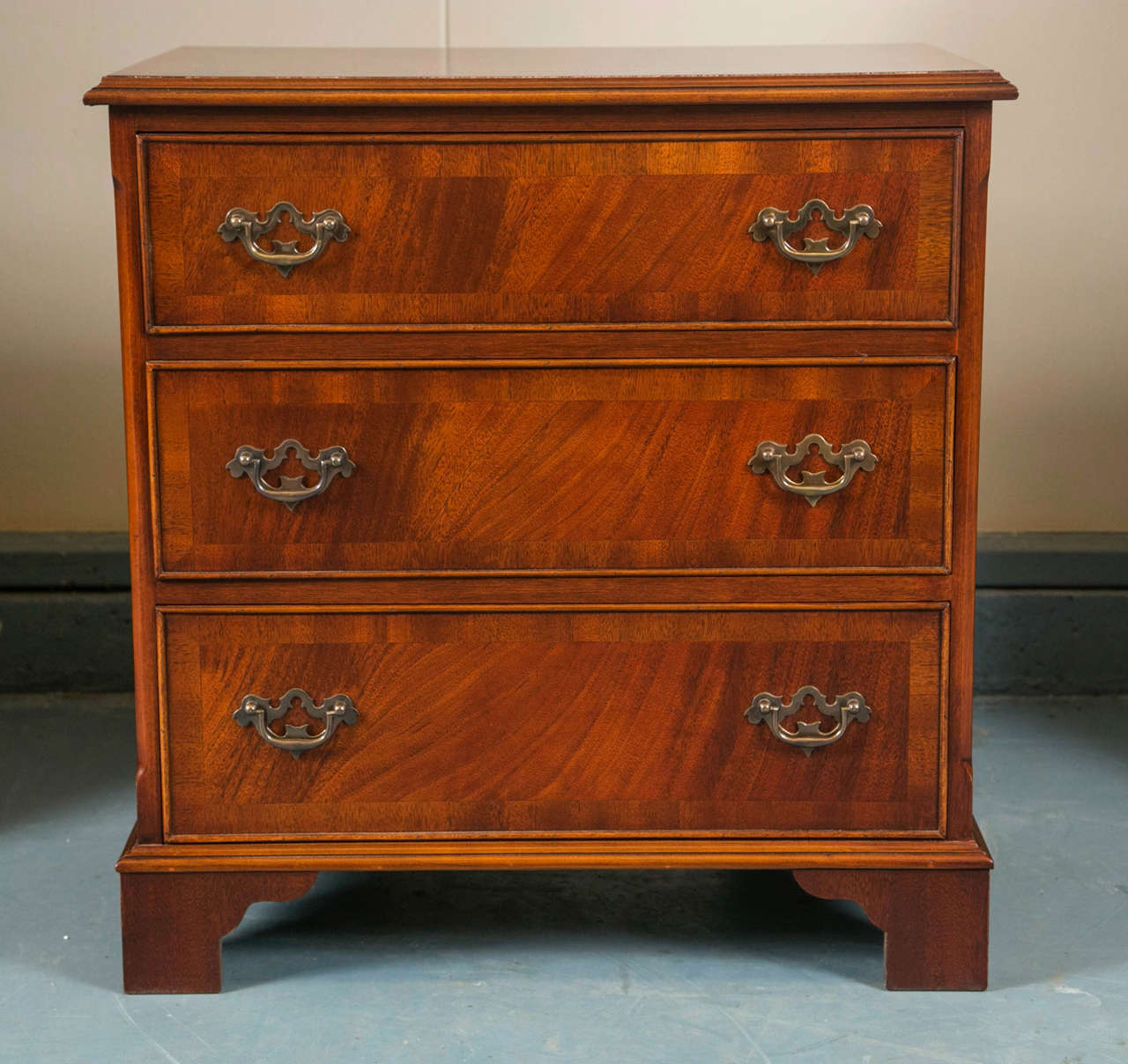 Custom made for us by English cabinet makers, this Classic little three-drawer chest in flame mahogany has chamfered corners and rests on bracket feet. The top and drawer fronts are cross banded in a sedate, straight grain mahogany that frames the