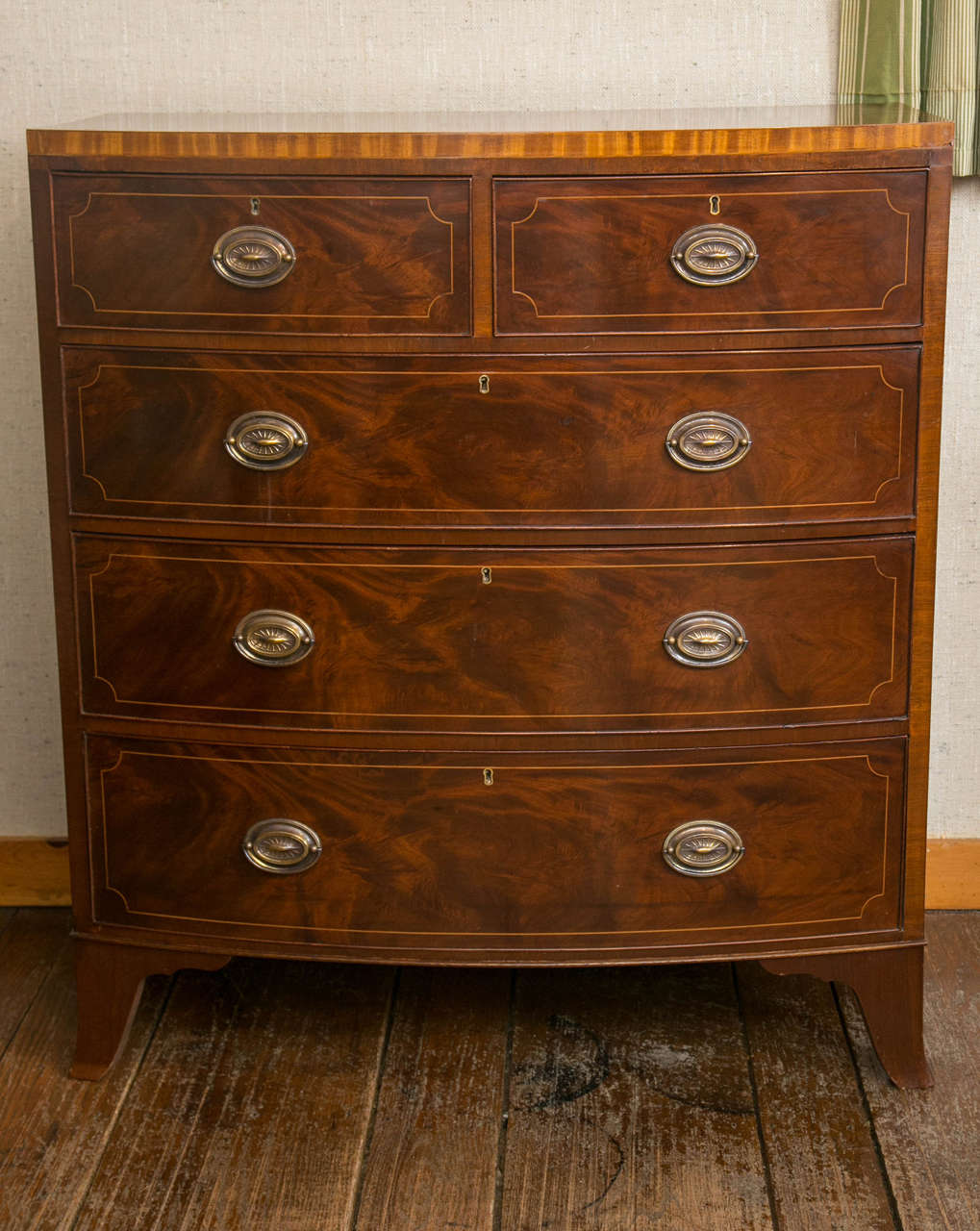 Not your garden-variety bow front chest (who would put a mahogany chest in the garden?), this chest has a string, contrasting band of satinwood the envelopes the top edge and string inlay on the drawer fronts. A traditional arrangement of two small