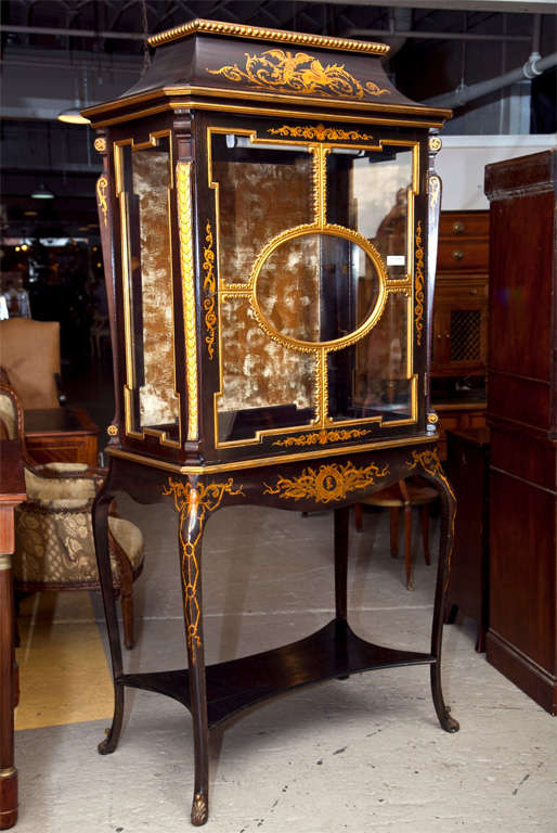 A charming Chinoiserie style curio cabinet, circa 1940s, overall ebonized with elegant hand-painted parcel-gilt detail. The pagoda styled top over a conforming glass case with velvet interior backdrop, supported on a table base raised by four