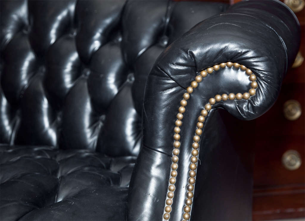 Pair of English Georgian style black chesterfeld sofas or loveseats, possibly 3rd quarter of 20th century, shaped back with rolled arms upholstered in tufted leather and buttons, decorated with original brass nail heads, raised on mahogany base with