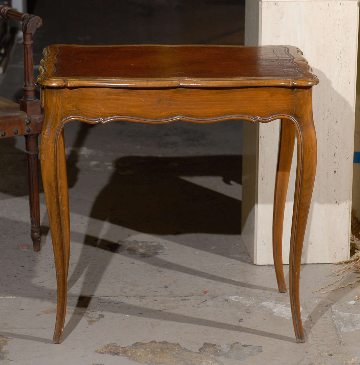 20th century French Louis XV style side table of walnut featuring a scalloped ogee edge top with a brown embossed leather inset.  The table holds one drawer, has a scalloped apron, and rests on cabriole legs.  Great condition.