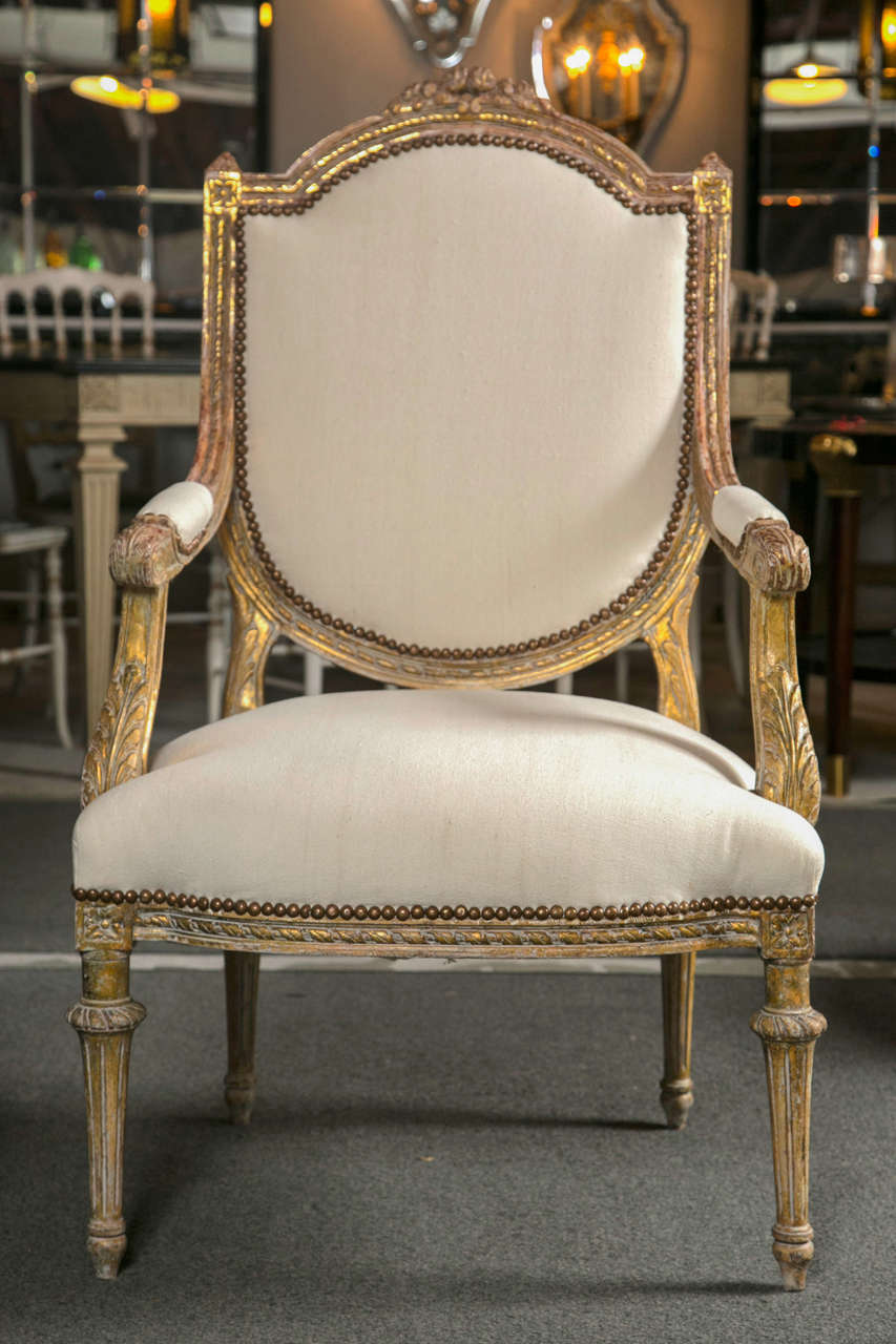 Pair of French fauteuils in the Louis Philippe style, circa 1940s with later upholstery and original brass studs. The shield-form back surmounted by distressed and annulate-carved frame, down-swept and padded arms, the apron under the seat having