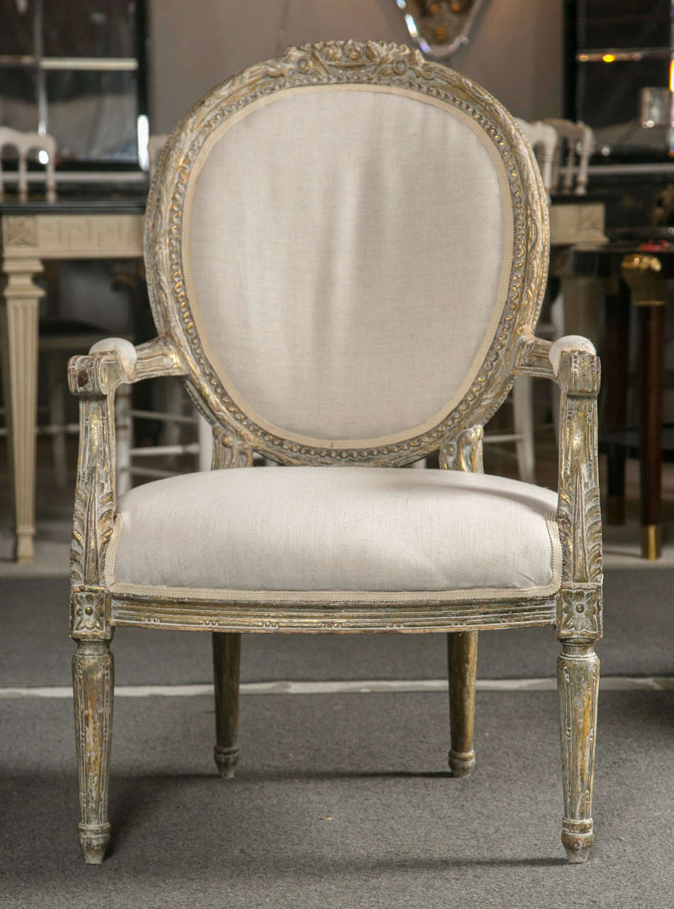 Pair of vintage French Louis XVI style fauteuils, circa 1940s with later upholstery, the oval padded back surmounted by intricately carved wood frame in a beautiful distressed finish, padded arms and ample padded seat, raised on tapering circular