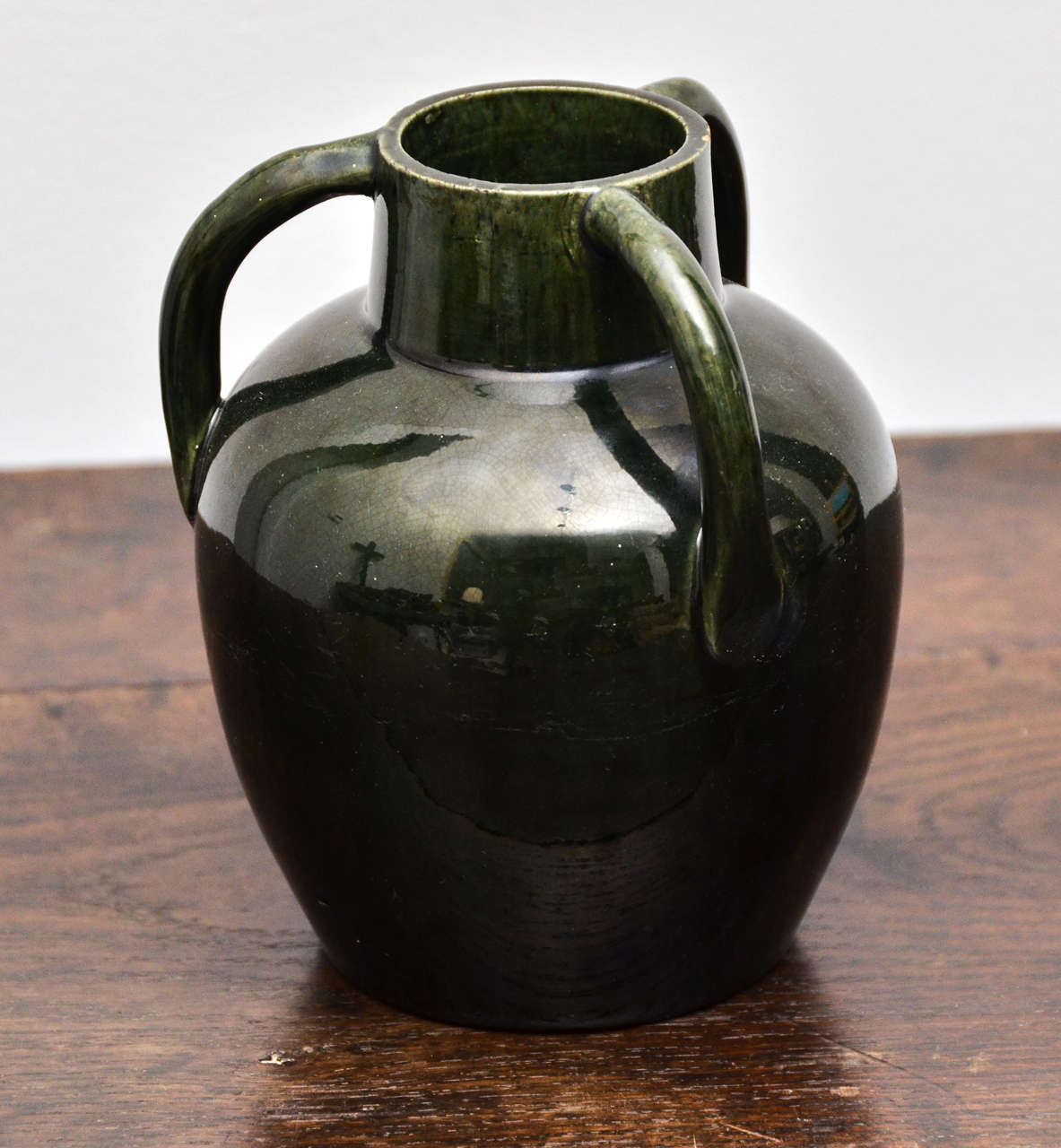 Dark green ceramic jug with high gloss glazing and three handles.