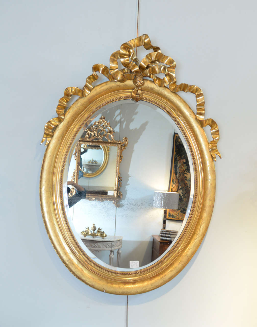 19th Century Louis XVI Gilt Mirror, Circa 1830
This gorgeous and graceful mirror has quite a presence.  The oval frame has a subtle and delicate etching in a flora and vine motif.  The proportions of the wide beaded frame and the elaborate bow that