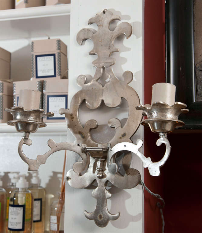 Originally candle sconces these two-arm sconces have been electrified. They have a scrolling fleur-de-lis design.