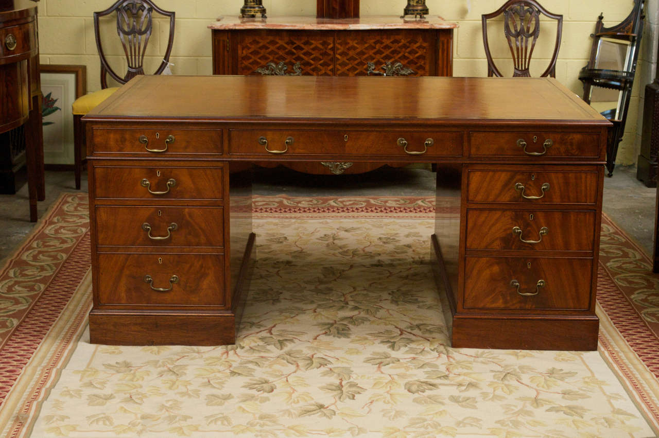 A beautiful flame mahogany George III style pedestal partners desk with brown embossed leather top. The top case has one long frieze drawer flanked by two smaller drawers on one side and three false drawers behind. The two pedestals each have one