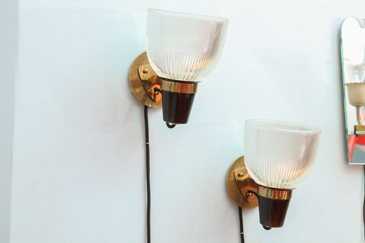 Frosted, ribbed glass shades.  Enameled steel and brass structures, and back plates.   these sconces are well documented and have been recently rewired.   This pair is an early version of this model.  They also have a custom circular back-plate (not