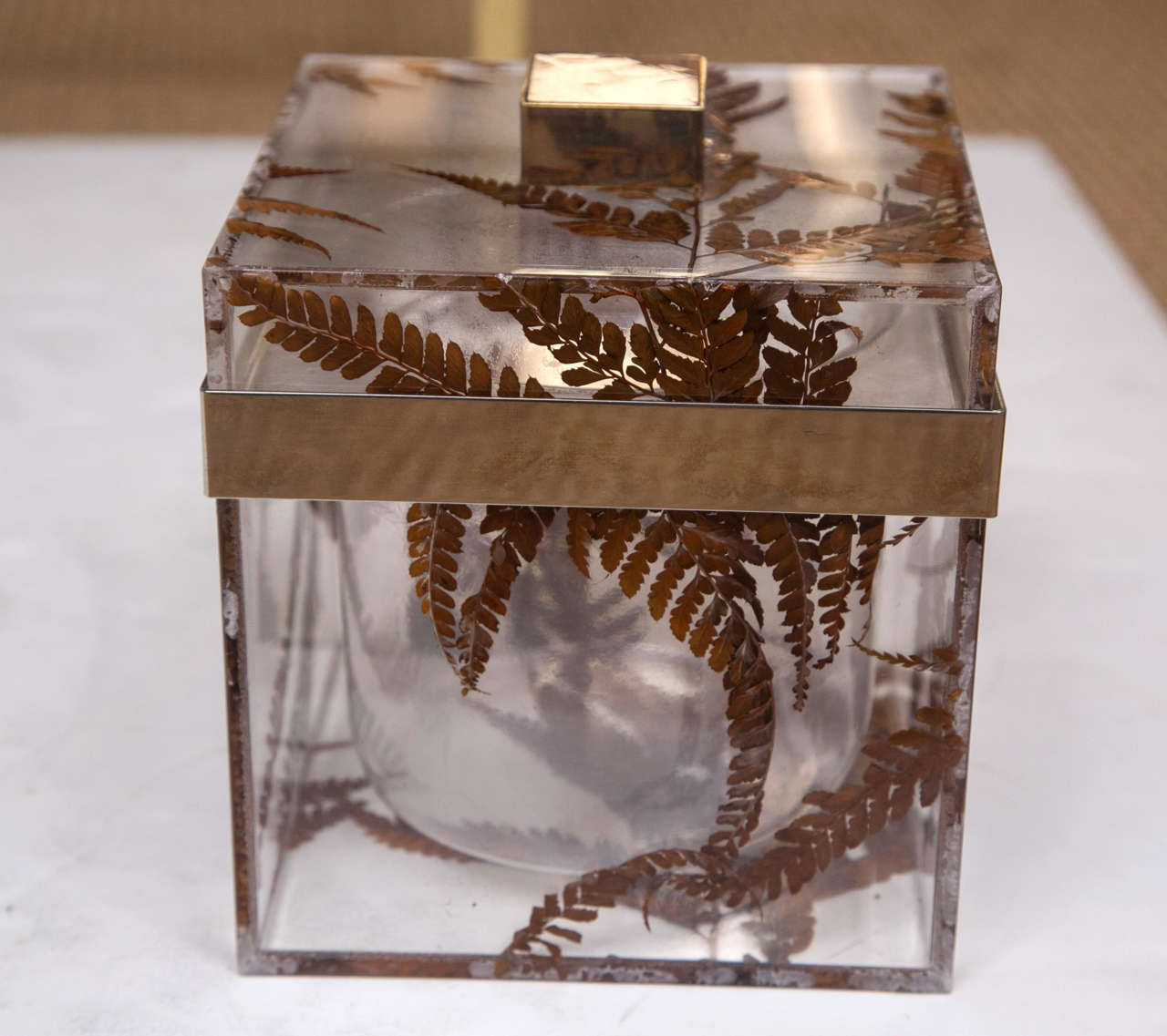 A cube form Lucite ice bucket with dried pressed leaves lining the outer walls.