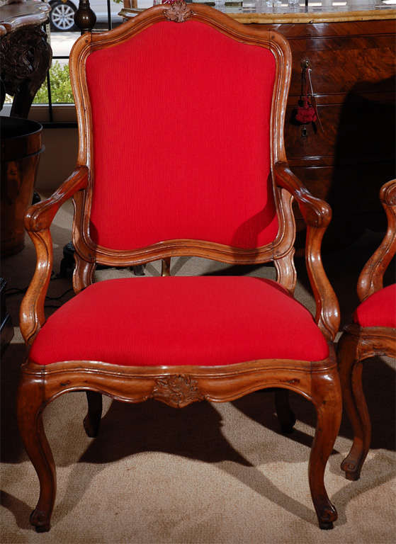 Pair of carved Italian walnut open arm chairs, with a shell cartouche , in red fabric