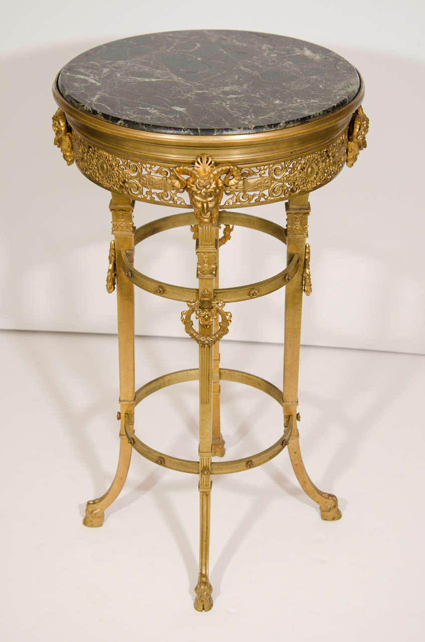 Cette spectaculaire table d'appoint circulaire en bronze doré est un exemple fantastique de design néoclassique. Cette table présente un plateau circulaire en marbre noir encadré par une galerie réticulée en bronze doré, décorée de motifs