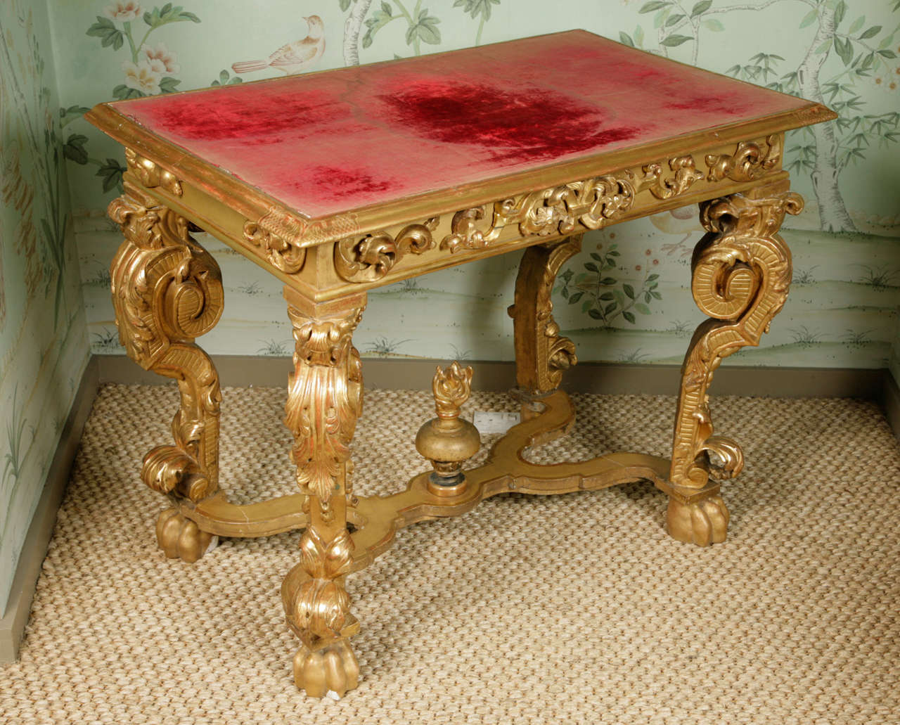 A finely carved gilt wood and gesso console table dating from the last quarter of the seventeenth century. The curvature of the legs, paw feet and stretcher surmounted by an urn are suggestive of an Italian origin. Table top covered in antique red