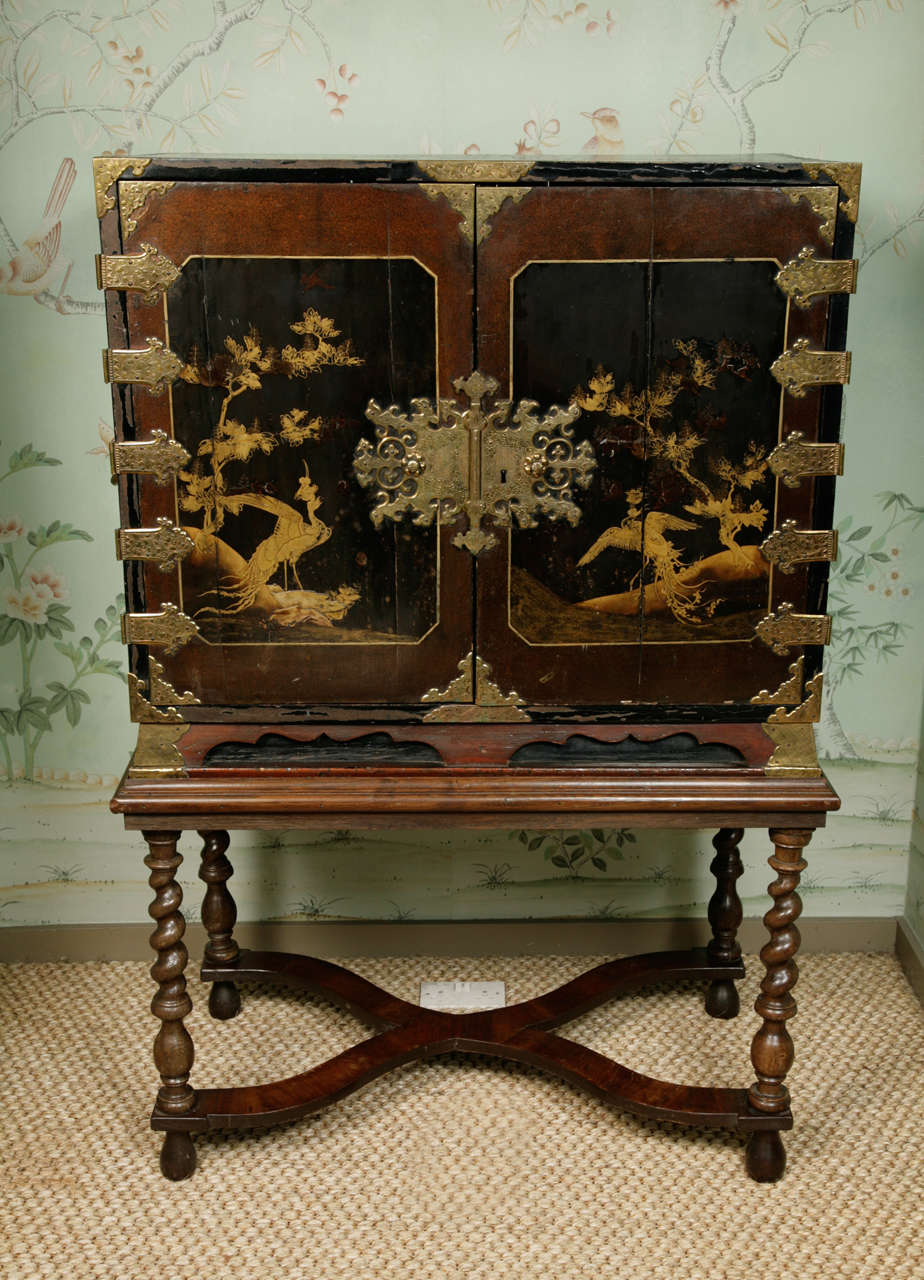 A 17th century Japanese lacquer cabinet on an English 17th century style stand incorporating period turned columns. The two doors which make up the front of the cabinet shows two central panels  which depicts phoenixes (a mythical symbolic bird in