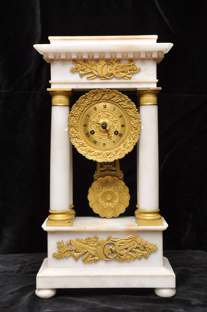 Exquisite Louis Philippe period hand carved alabaster, portico clock supported on four tapered columns to a raised plinth base, each column has gilt bronze mountings, gilt bronze relief at crest and base, each depicting musical instruments. Key wind