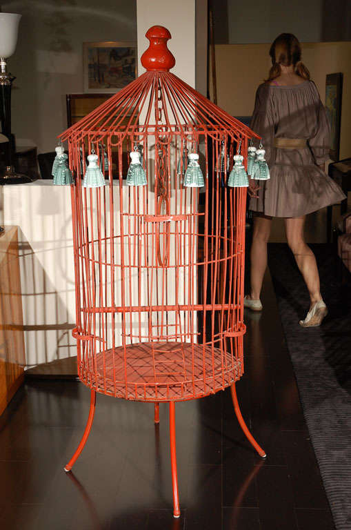 Unique oversized metal bird cage at 5 foot 4 inches tall. The frame is painted in crimson red with decorative green tassels in casting plaster handing from the hat. Done by American artist Tony Duquette. 