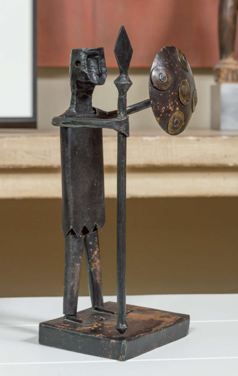 A cartoonish mid-20th century Mexican iron and brass detailed sculpture of a battle ready warrior