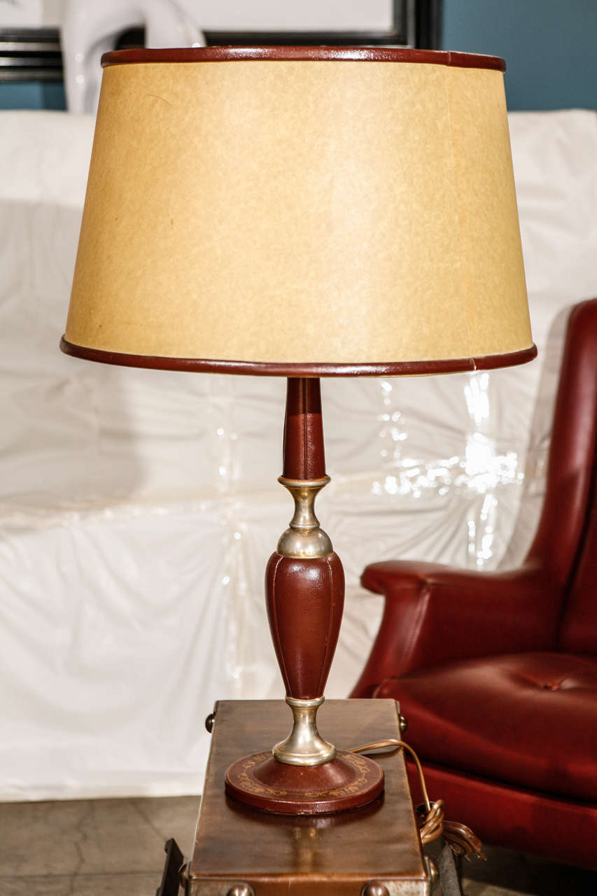 A classic Le Tanneur table lamp with its original matching leather trimmed shade. Made with burgundy leather with a gilded vine garland design around the base and brass connectors. Stamped underneath the base 
