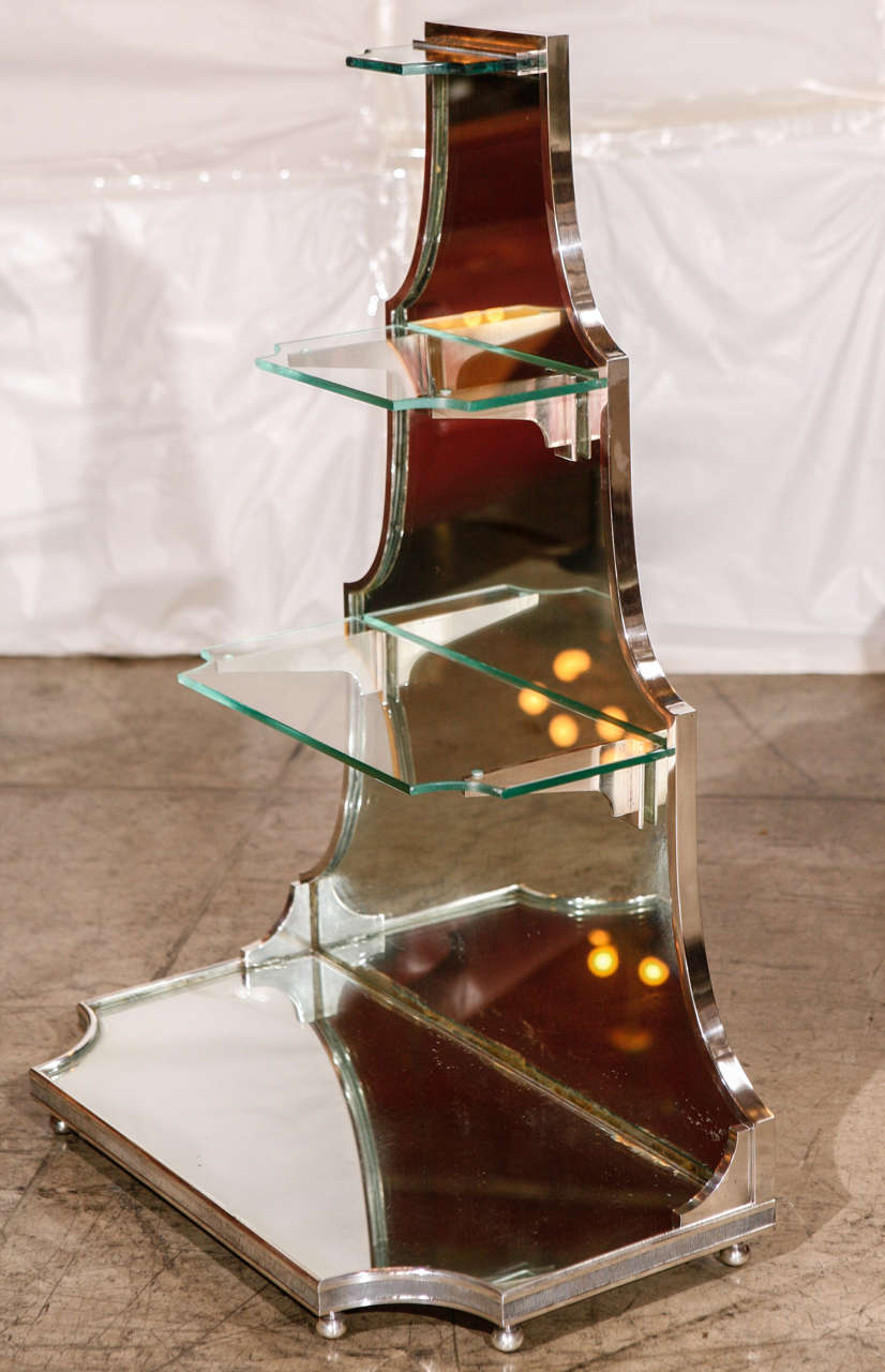 A unique French Art Deco display stand from the 1930s. Has four levels (three glass ones and one bottom mirrored one), sits on elegant ball feet and back is wood (painted off white). Mirror is original and bottom mirrored shelf has some corner chips