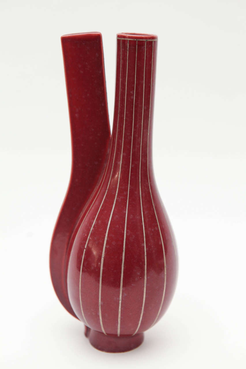 A surrealist split vase by Wilhelm Kage for Gustavsberg Porcelain in a mottled oxblood glaze with silver stripes. Marked on the bottom with the Gustavsberg anchor logo and 