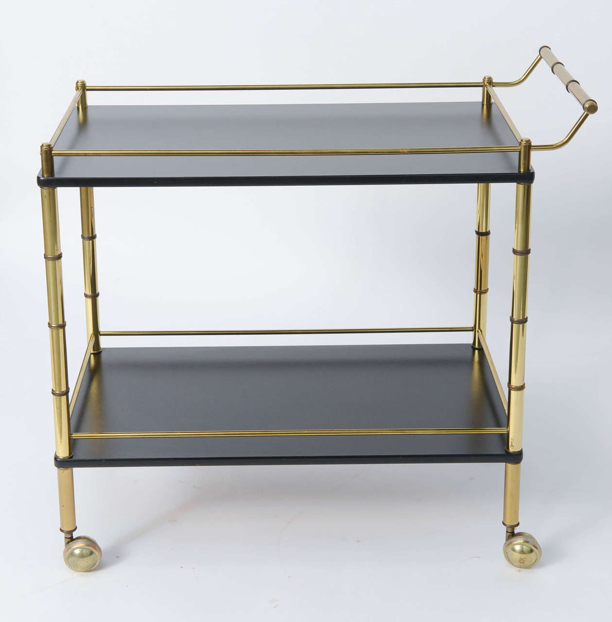 Stylish and quite utile, this 1950s-1960s bar or tea cart makes a fine and elegant statement whether parked or serving on the move. Brass with a faux bamboo motif, black lacquered top and bottom levels, both with brass rod gallery edges all on