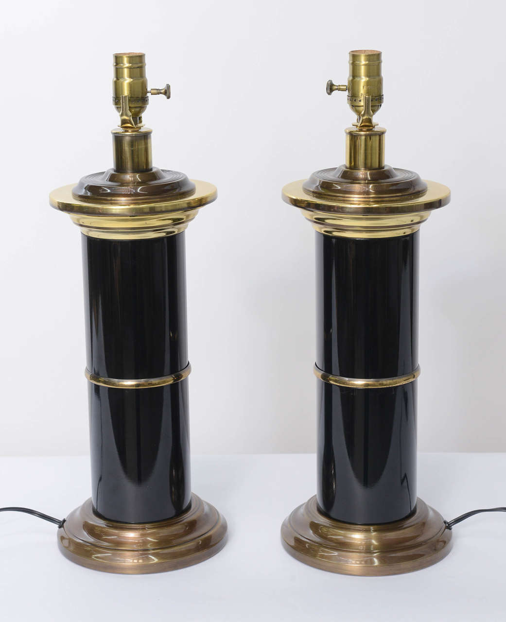 Quite elegant and sleek, strong and masculine, this pair of modern Empire style table lamps has a wonderful fat column of black lacquered brass with stepped circular base, centre brass belt and column capital of multi-stepped brass. Rich and with a