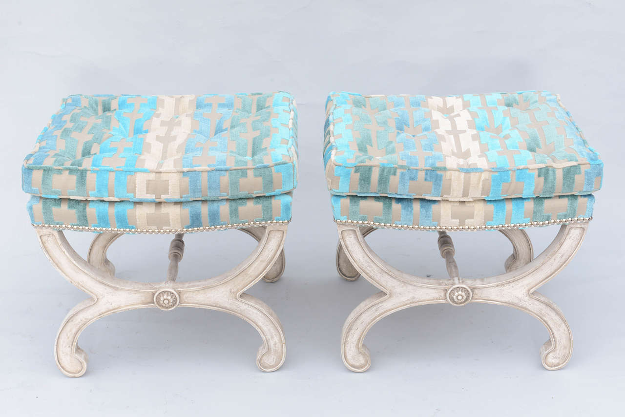 Pair of curule benches, or ottomans, each having X-frame in distressed painted finish, carved with rosettes, upholstered in cut chenille fabric with silver-finish nailheads.

Stock ID