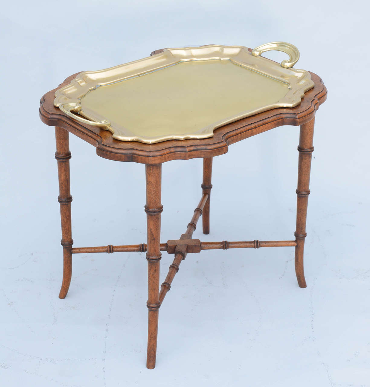 Tray table, having serpentine shaped brass tray with handles, inserted in conforming walnut frame, raised on faux bamboo legs with X-stretcher.