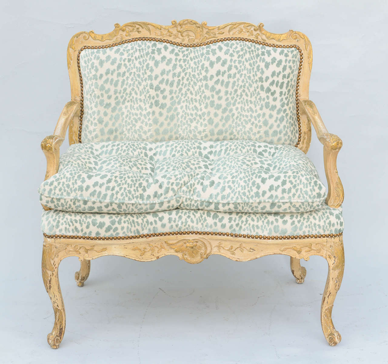 Small settee or loveseat, having a painted and parcel gilt frame, finely carved with foliate and scrollwork, with natural wear; its scroll armrests raised on downswept terminals, padded seat holding a loose down-filled cushion, similarly carved