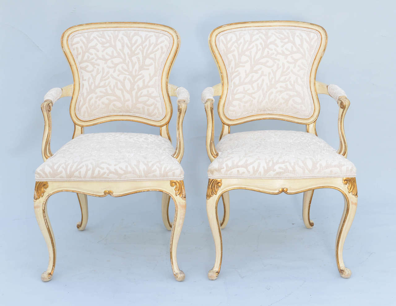 Pair of Venetian style armchairs, each having a painted frame with parcel gilt details; free-form shaped padded back in channeled frame, scrolling arms with elbow pads, on down-swept terminals, its seat on serpentine apron, raised on cabriole legs