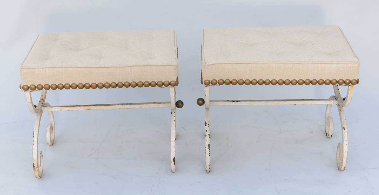 Pair of stools/benches, of wrought iron, with distressed painted finish; each having a rectangular boxed seat, upholstered with nailheads, on scrolling X-frame legs, joined by bar stretcher, accented with gilded balls.

Stock ID: D9394