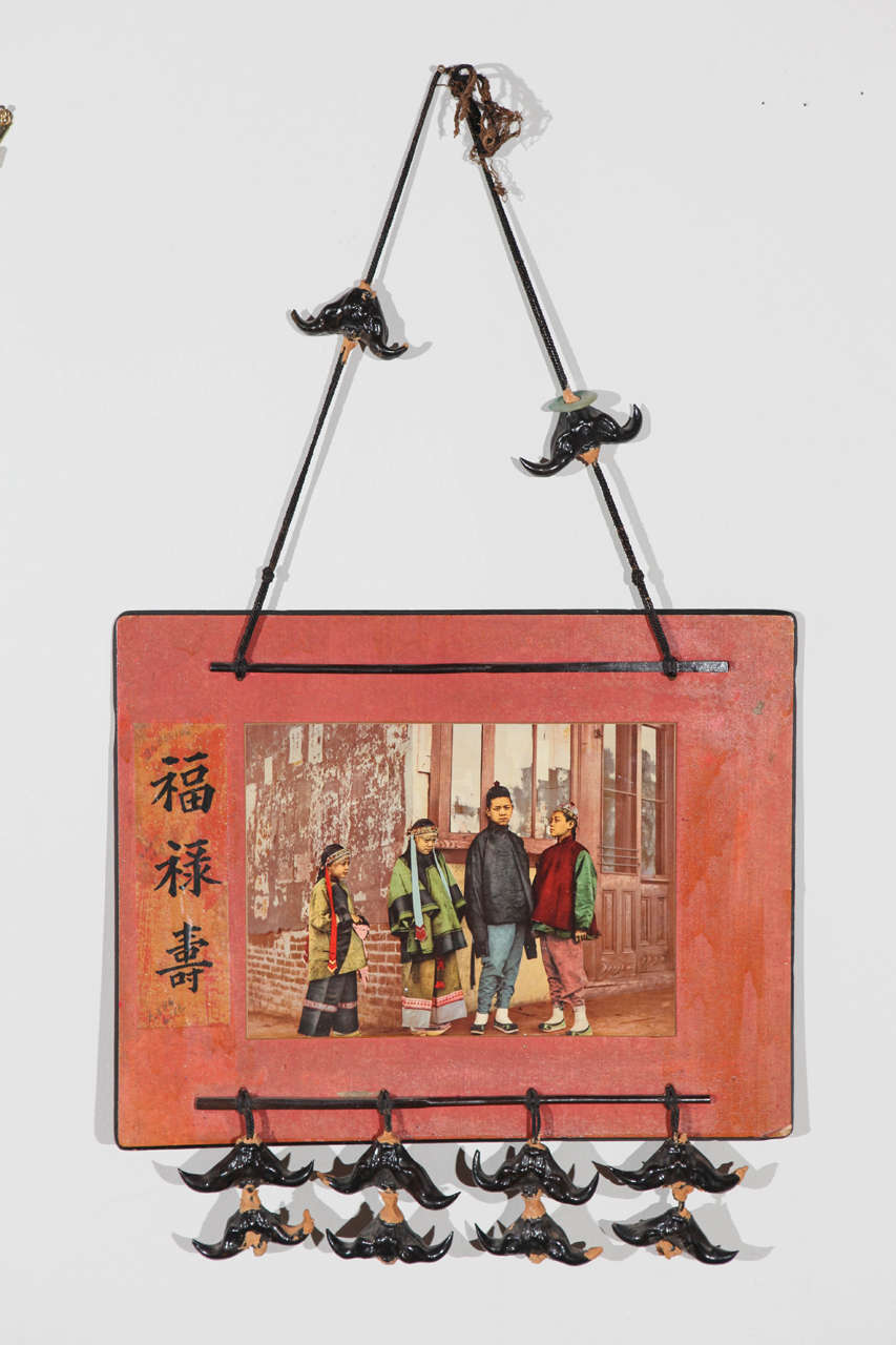 Early 20th century photo of Chinese children mounted on board with decorative terracotta details hanging on black fabric cords.