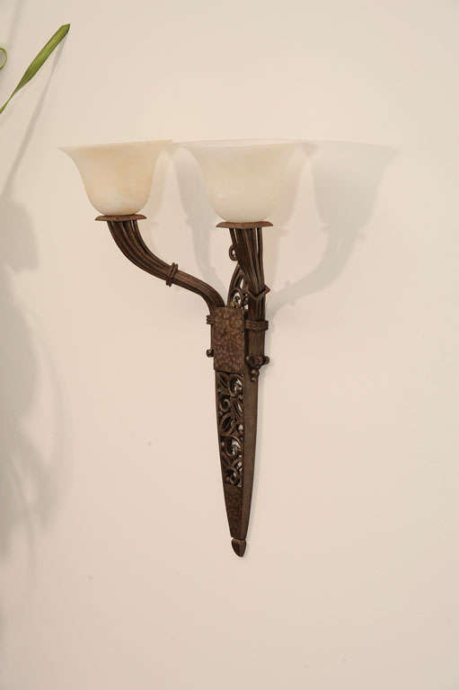 Une paire d'appliques Art Déco à deux lumières en fer forgé et albâtre par Paul Kiss avec des abat-jour en forme de trompette et des supports muraux percés de feuillages.