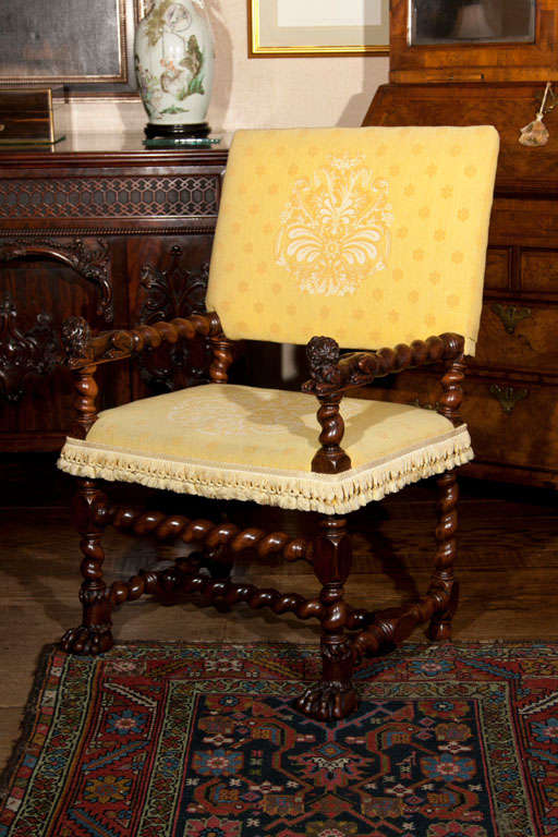 This regal seat dates to the 16th century. The square seat and back contrasted by the blocked barley twist turnings that comprise the arms legs and stretcher. Well-carved recumbent lions terminate the arms and the hairy paw feet complete the theme.