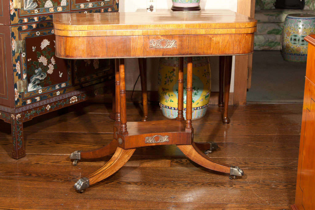 An attractive example of an English pedestal game table with four column support and bronze embellishment. Top and legs are inlaid with brass stringing and the deeply splayed legs end in brass 