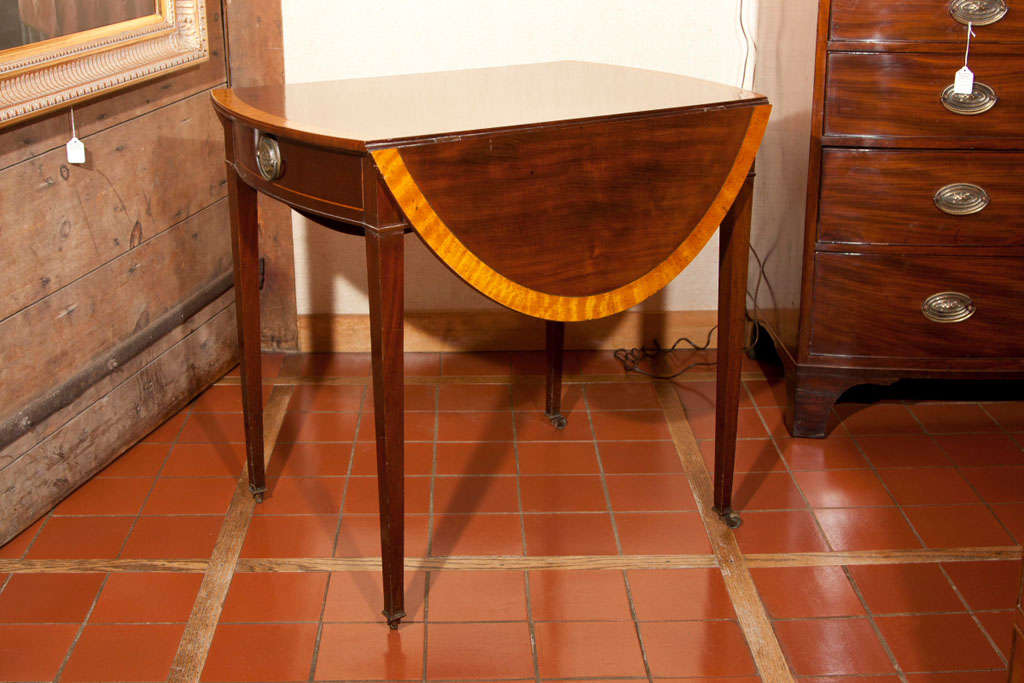 This feisty little mahogany Pembroke has all the right touches. Its bright satinwood cross banding announces its presence and the satinwood string on the bowed drawer front echoes the sentiment. The tapered legs lead the eye down to ever-so-delicate